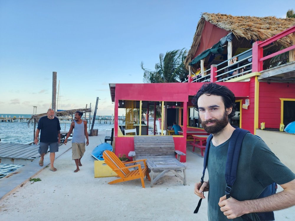 Owen standing on a sandy beach path in Caye Caulker, Belize, wearing a backpack