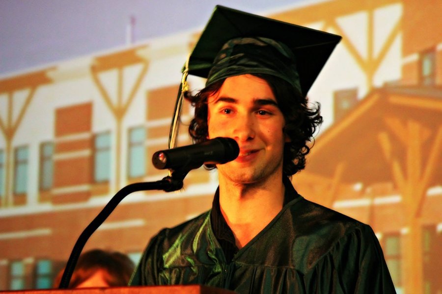 Owen in a cap and gown speaking at a microphone during his high school graduation