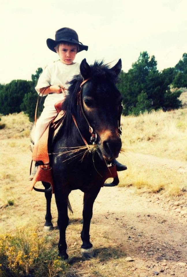 Owen as a young child riding a black pony wearing a cowboy hat in a dry mountain landscape