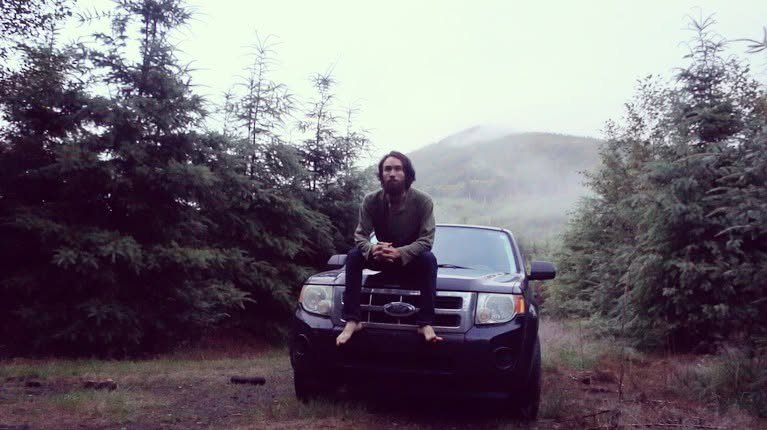 Owen sitting on the hood of his car in a foggy forest clearing during his road trip