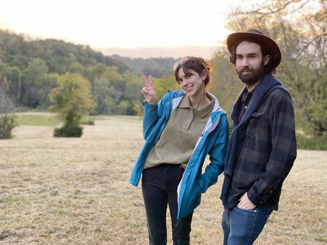Owen and his sister Elia smiling in a field near a forest at sunset